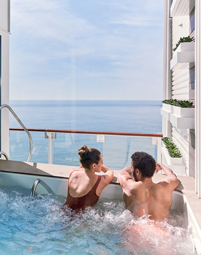 Two guests seated in a veranda plunge pool on a cruise ship with clear ocean views